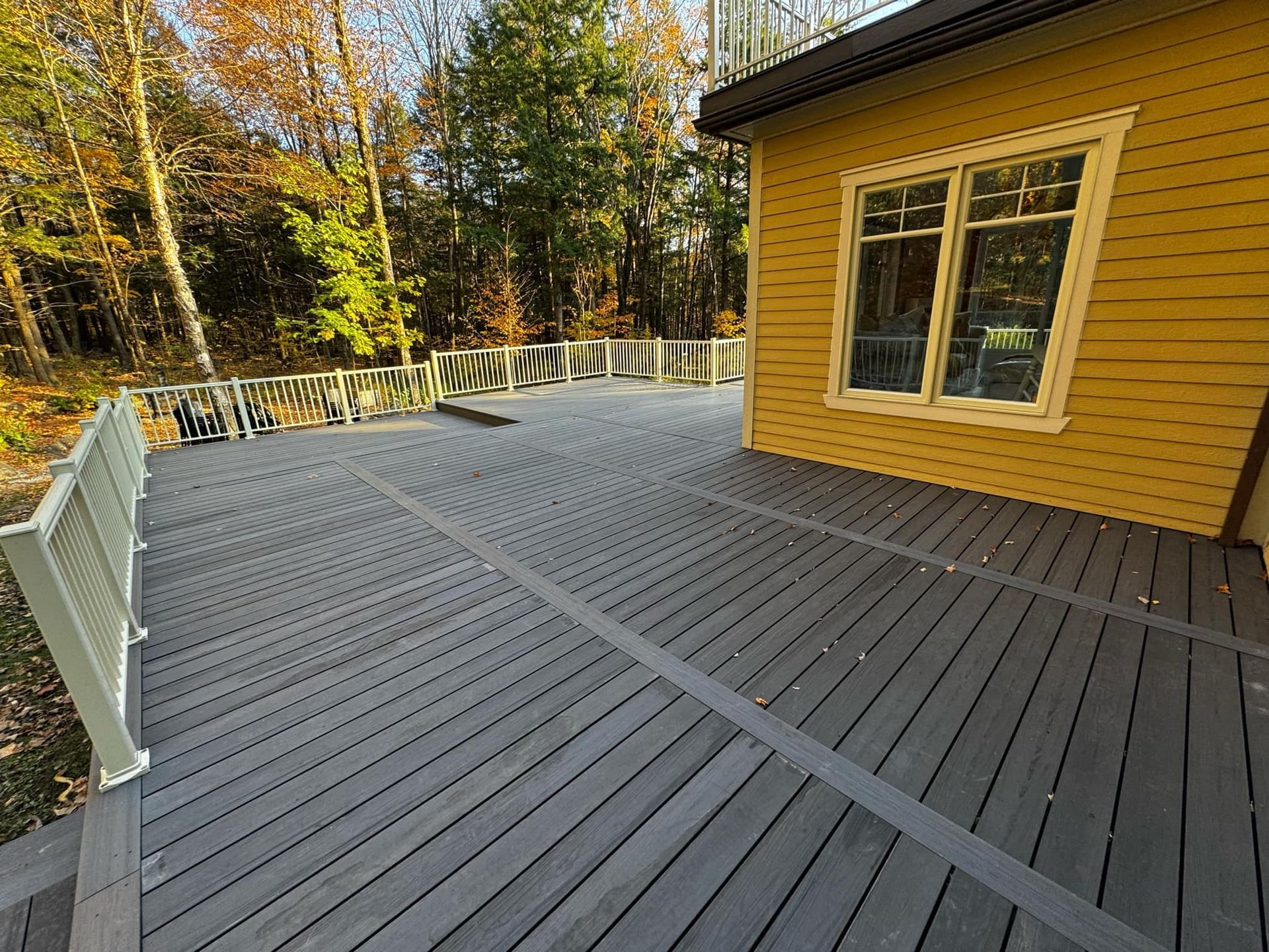 Une grande terrasse en bois se trouve devant une maison jaune.