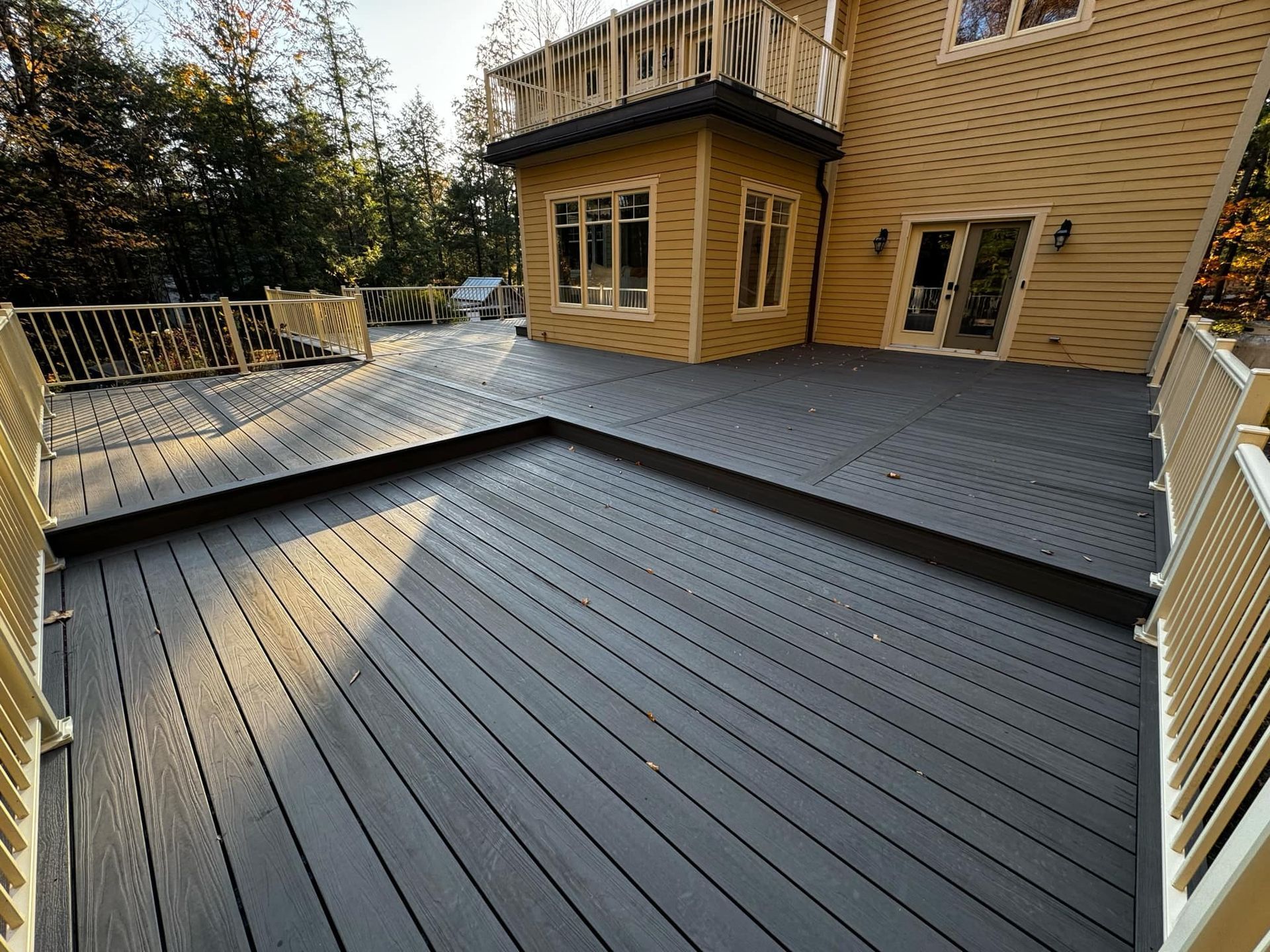 Une grande terrasse en bois avec une maison jaune en arrière-plan.