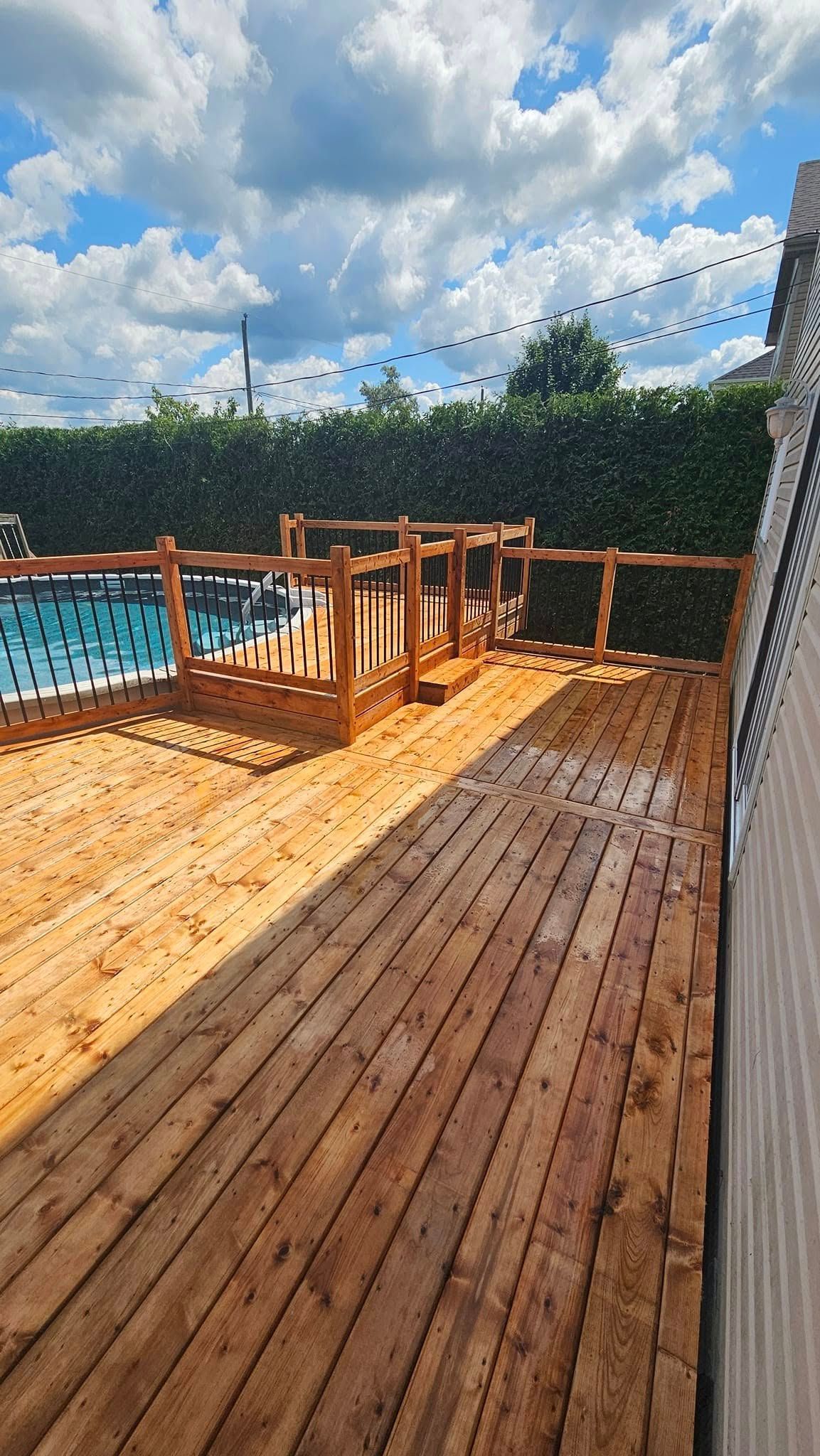 Une terrasse en bois avec une piscine en arrière-plan.