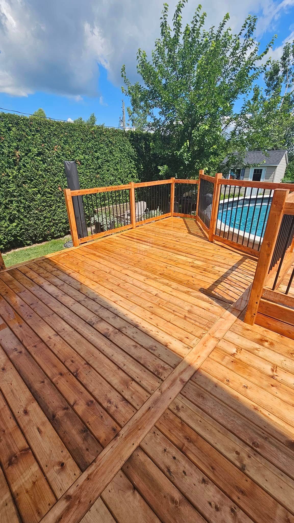 Une terrasse en bois avec une piscine en arrière-plan.