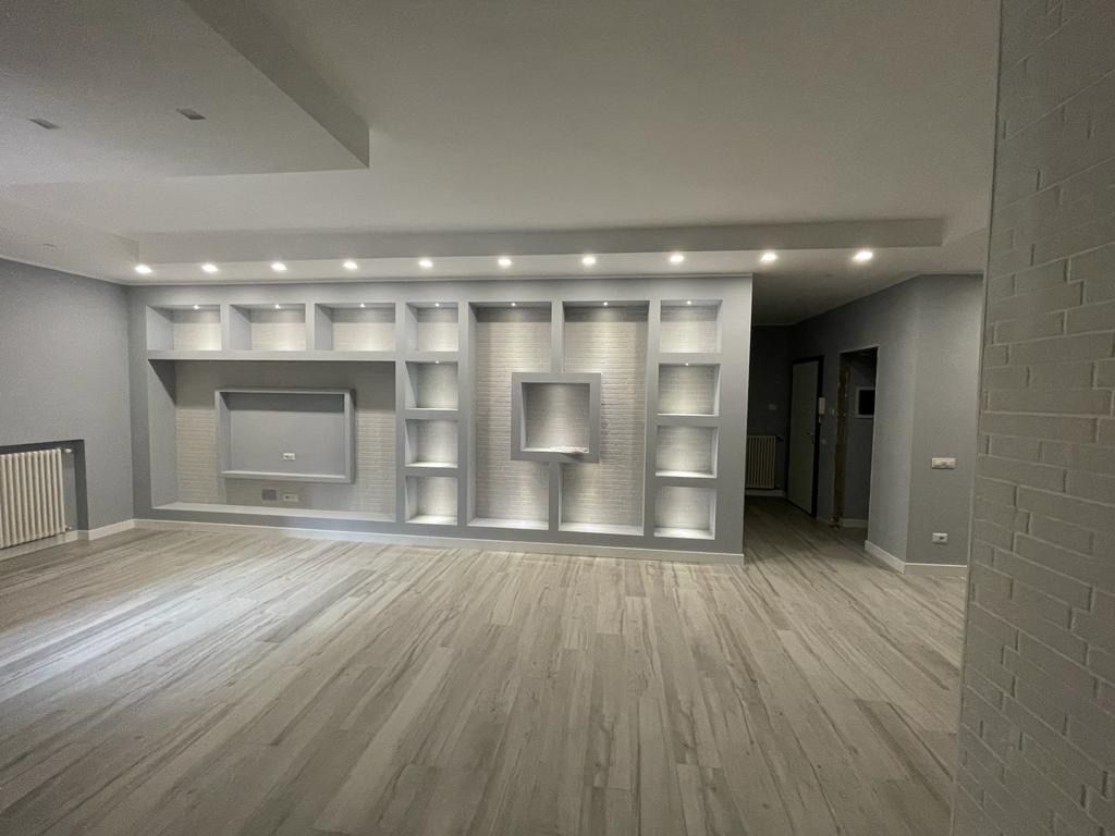 Un soggiorno vuoto con pavimenti in legno e una TV montata a parete.