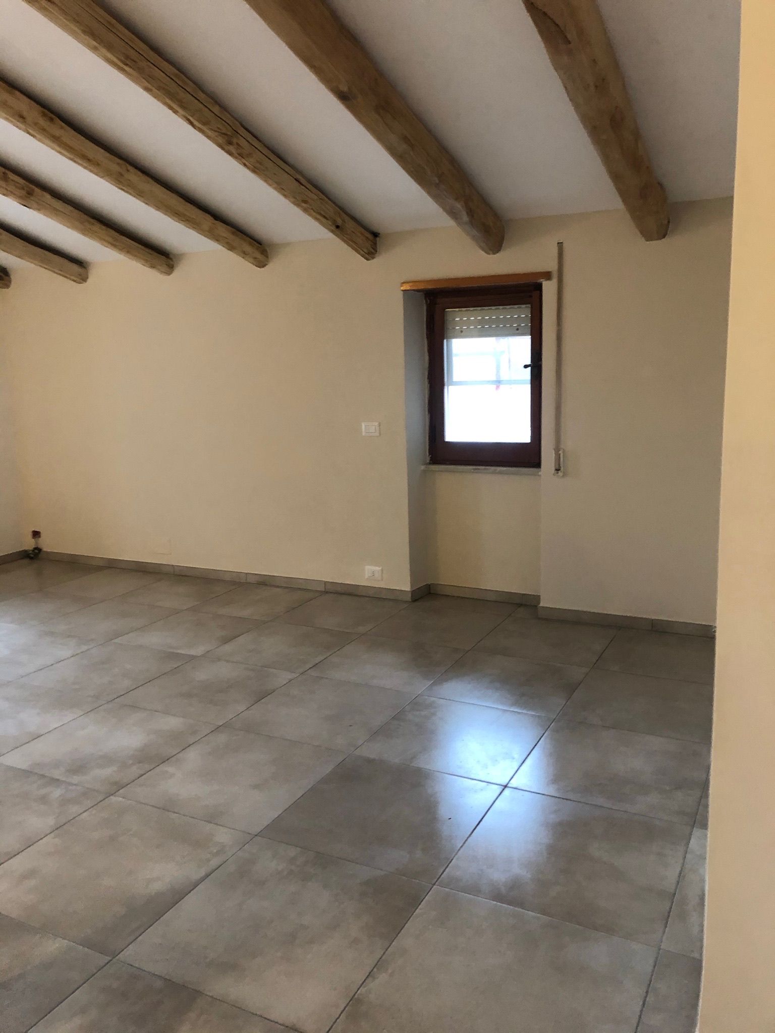 Una grande stanza vuota con pavimenti in piastrelle e travi in ​​legno.