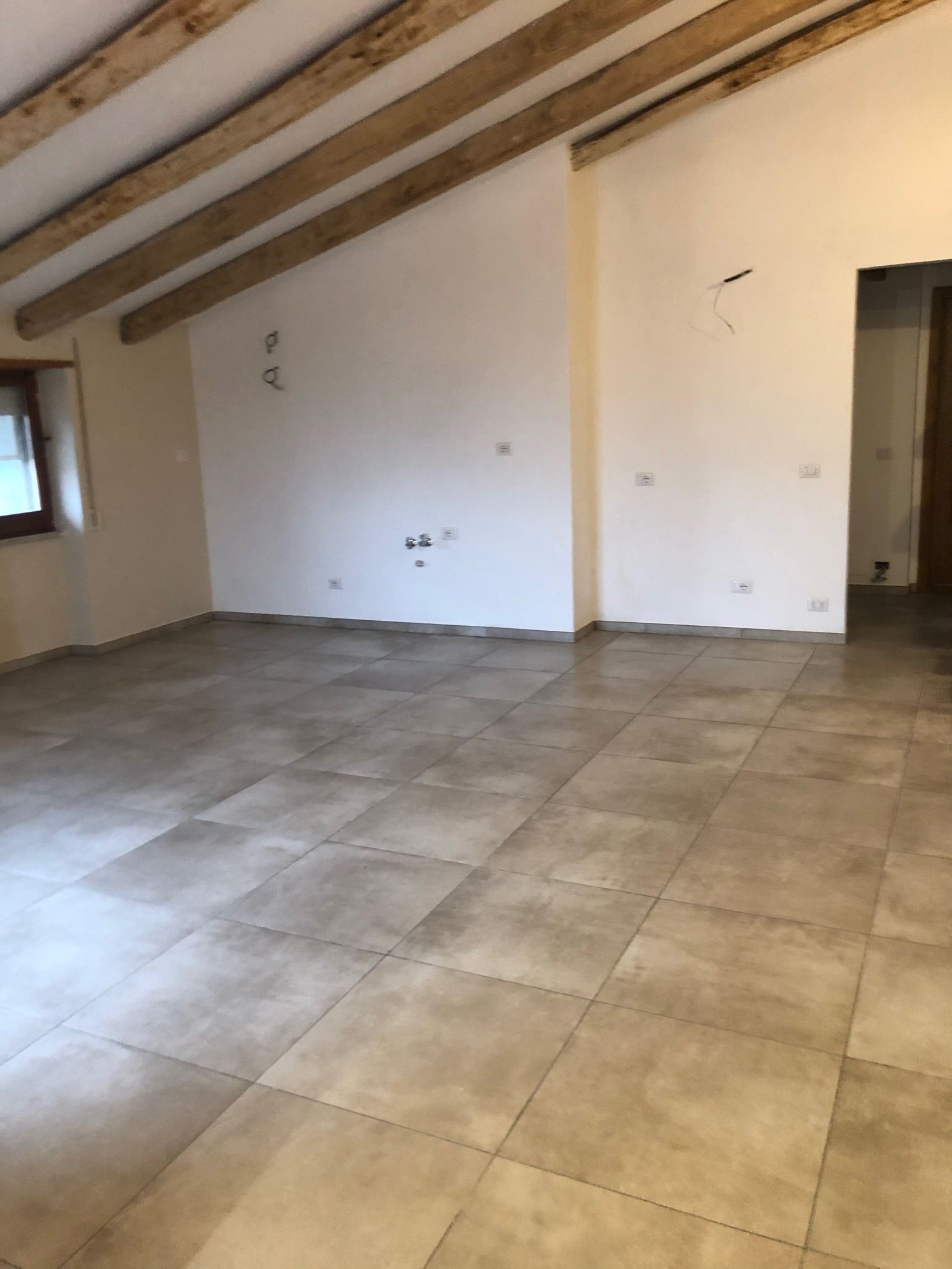 Una stanza vuota con pavimento piastrellato e travi di legno sul soffitto.