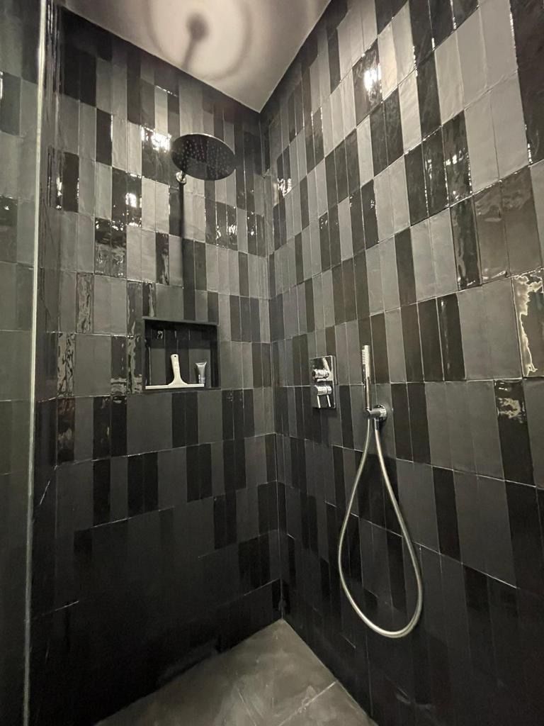 Una doccia con piastrelle nere e soffione.