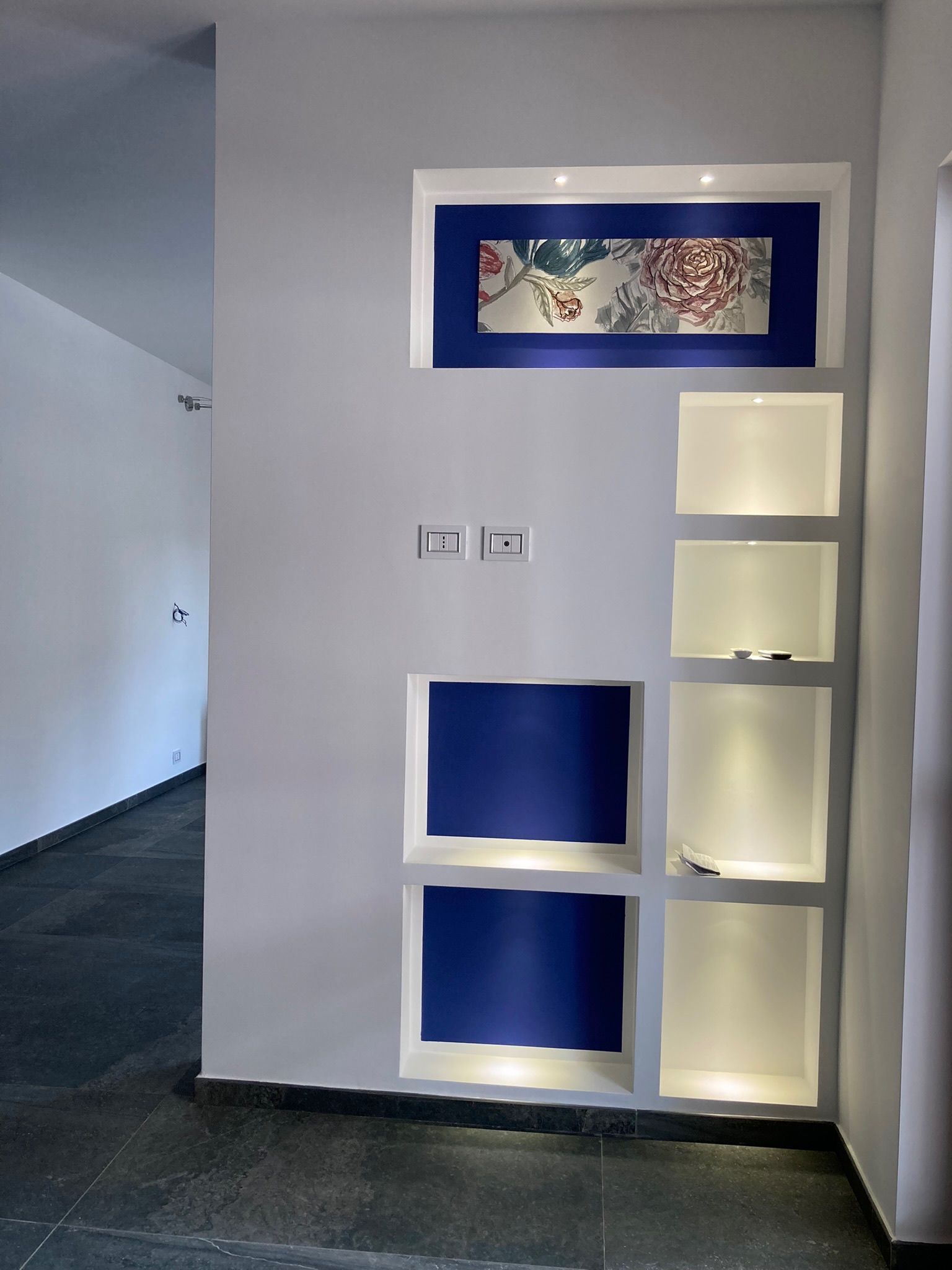 Un muro bianco con mensole blu e un quadro sopra