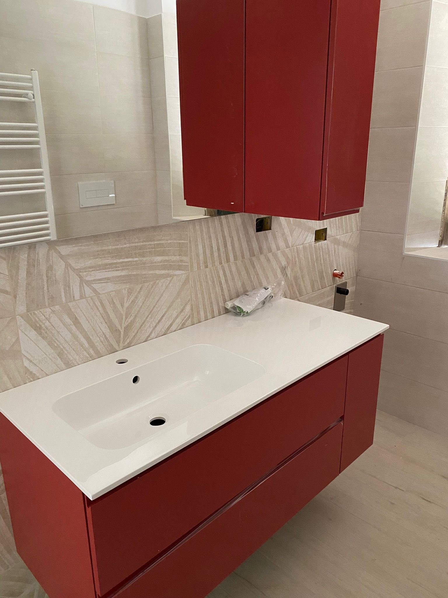 Un bagno con mobiletto rosso, lavandino, specchio e portasciugamani.