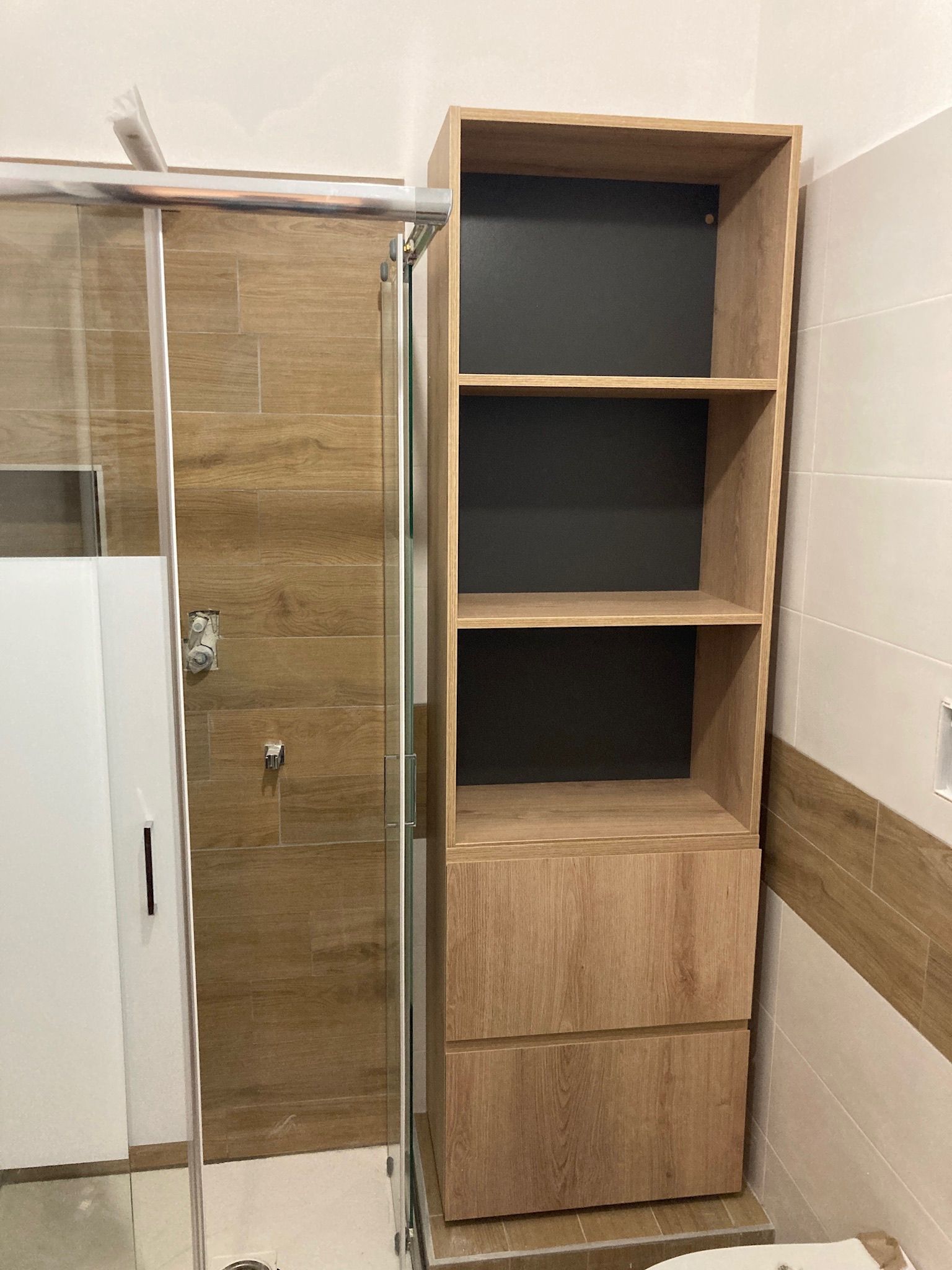 Un bagno con una mensola in legno e cassetti accanto a una cabina doccia.