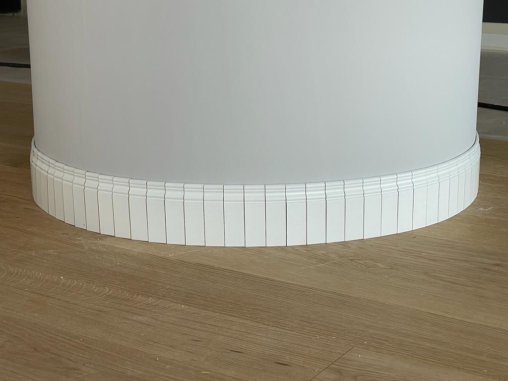 Un pilastro bianco con una modanatura bianca attorno è appoggiato su un pavimento di legno.