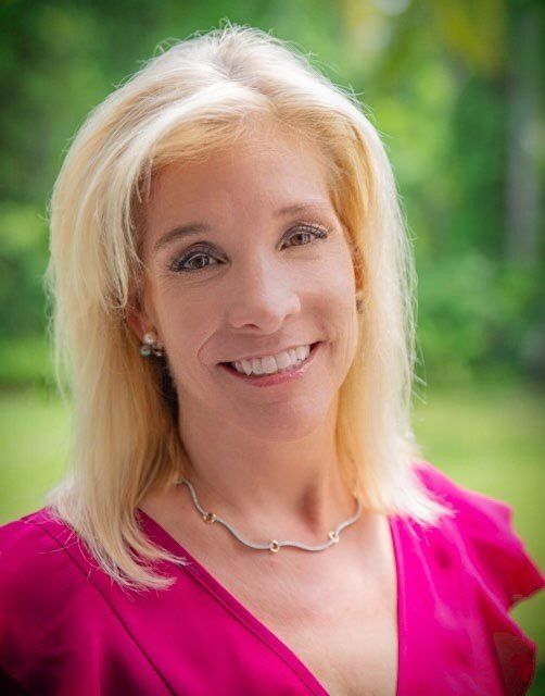 A woman in a pink shirt and necklace is smiling for the camera.