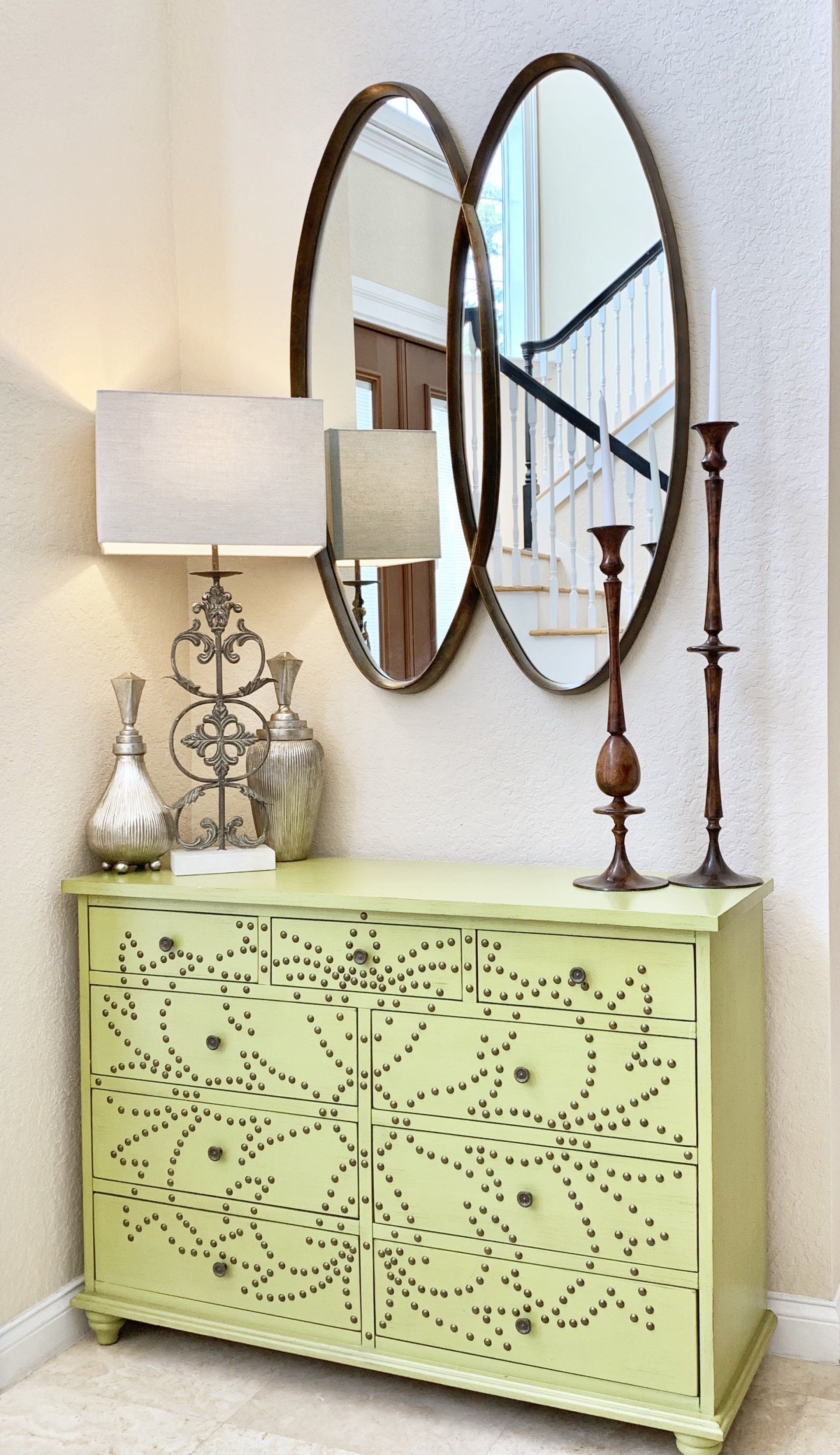 A green dresser with two mirrors above it