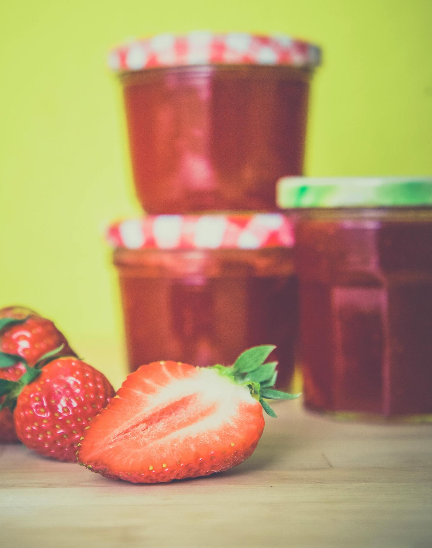 Strawberries and jars of jam on a wooden surface with a yellow background.