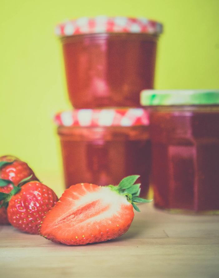 Strawberries and jars of jam on a wooden surface with a yellow background.