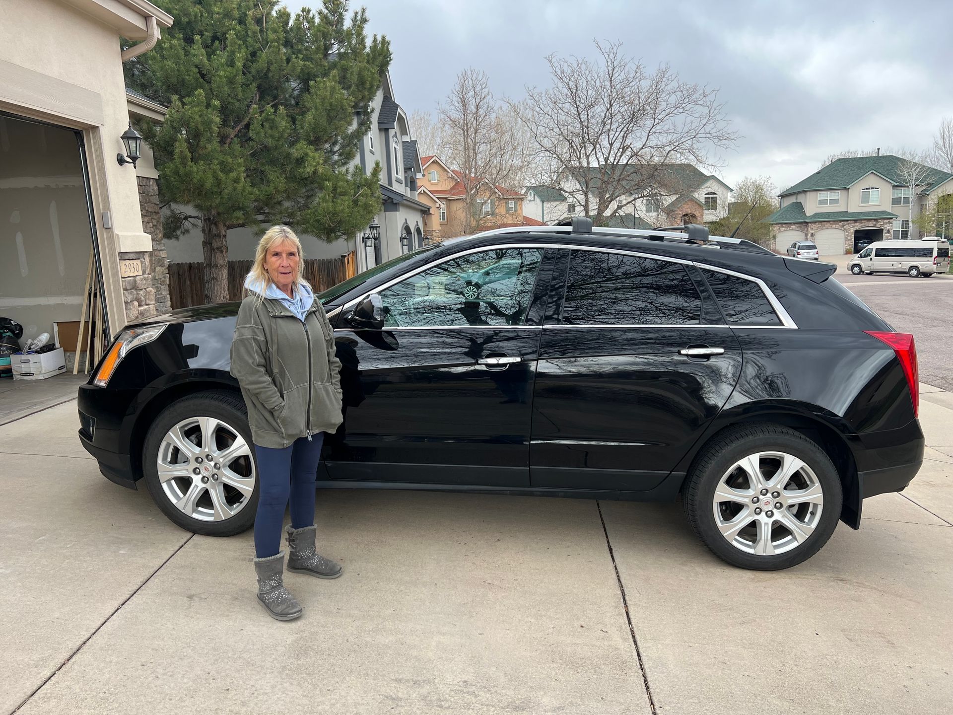A woman is standing next to a black car in a driveway.