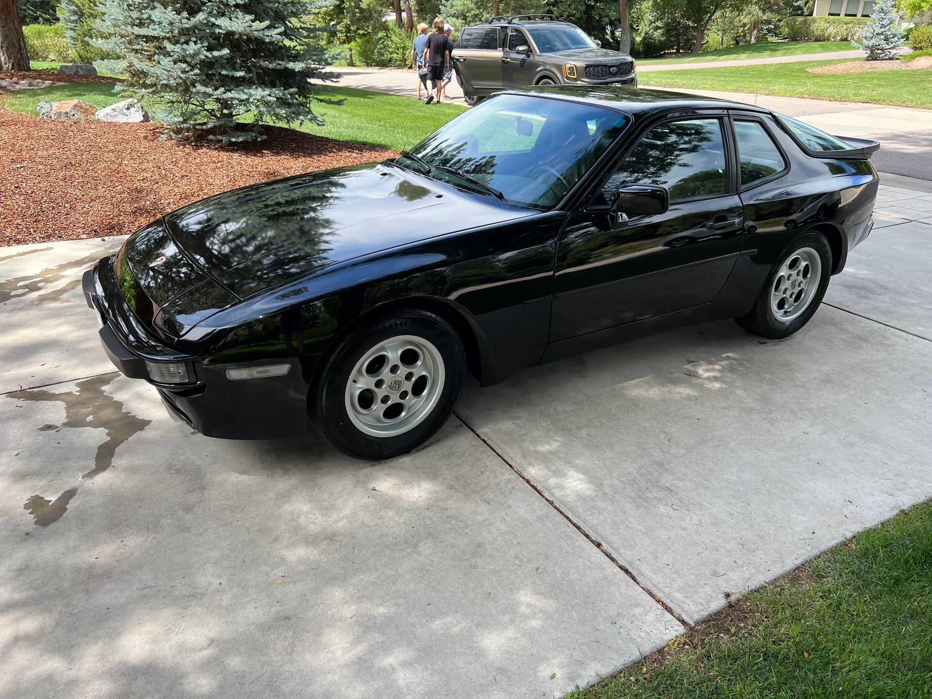 A black porsche 944 is parked on the side of the road.