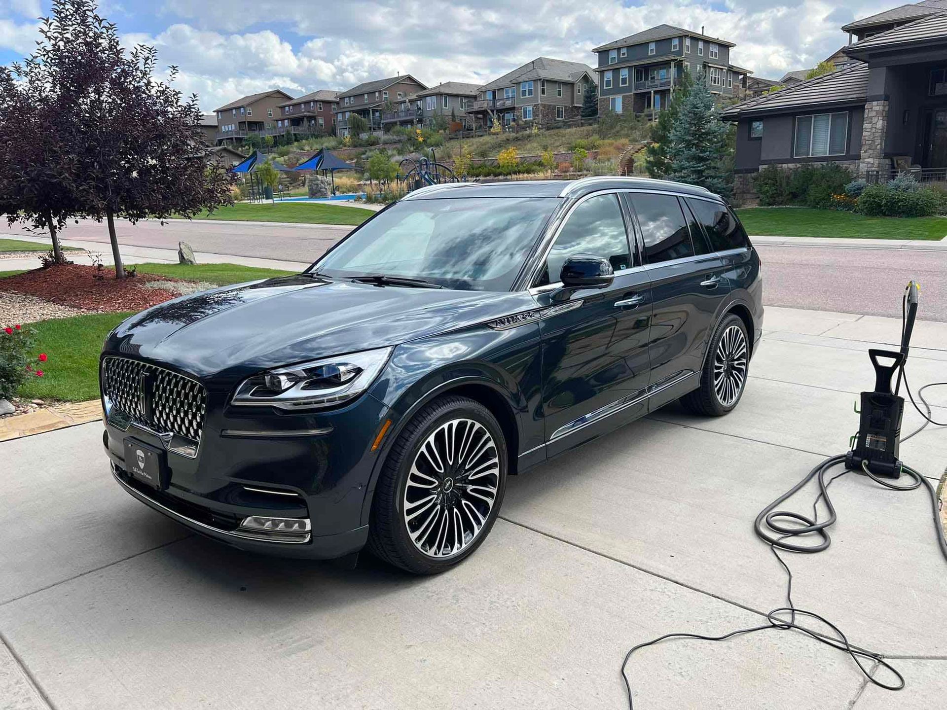 A black car is parked in a driveway next to a vacuum cleaner.
