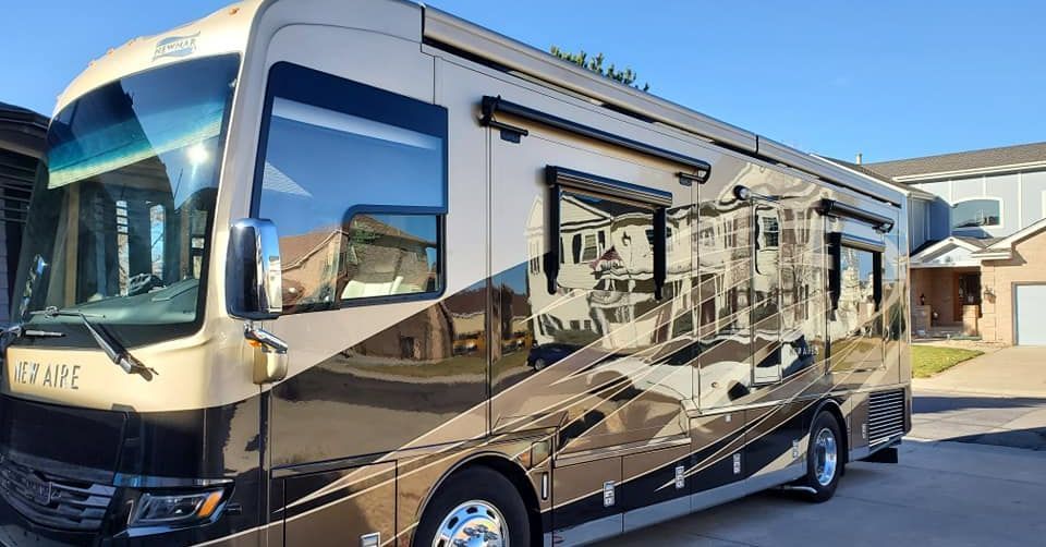 A large rv is parked on the side of the road in front of a house.