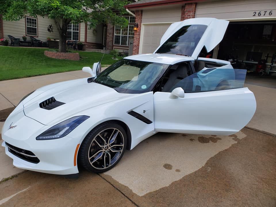 A white sports car is parked in a driveway with the hood up.