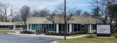 Single-story office building with glass doors, leafless trees, and a sign out front in a suburban lot
