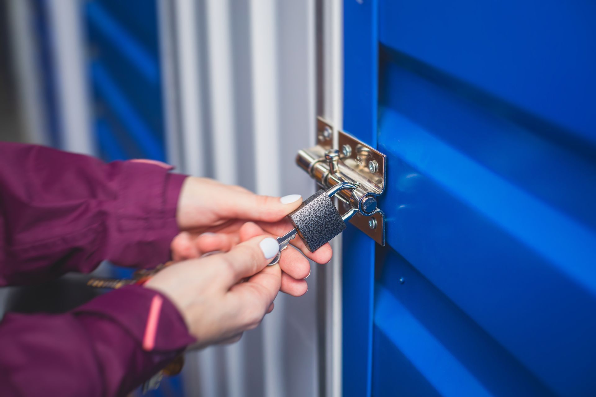 Hands locking a blue storage unit door with a padlock and key. Hands locking a blue storage unit door with a padlock and key.