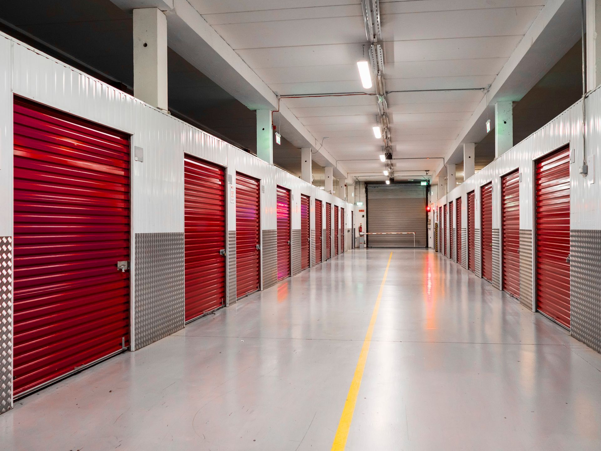 Indoor self-storage hallway with rows of red roll-up units.