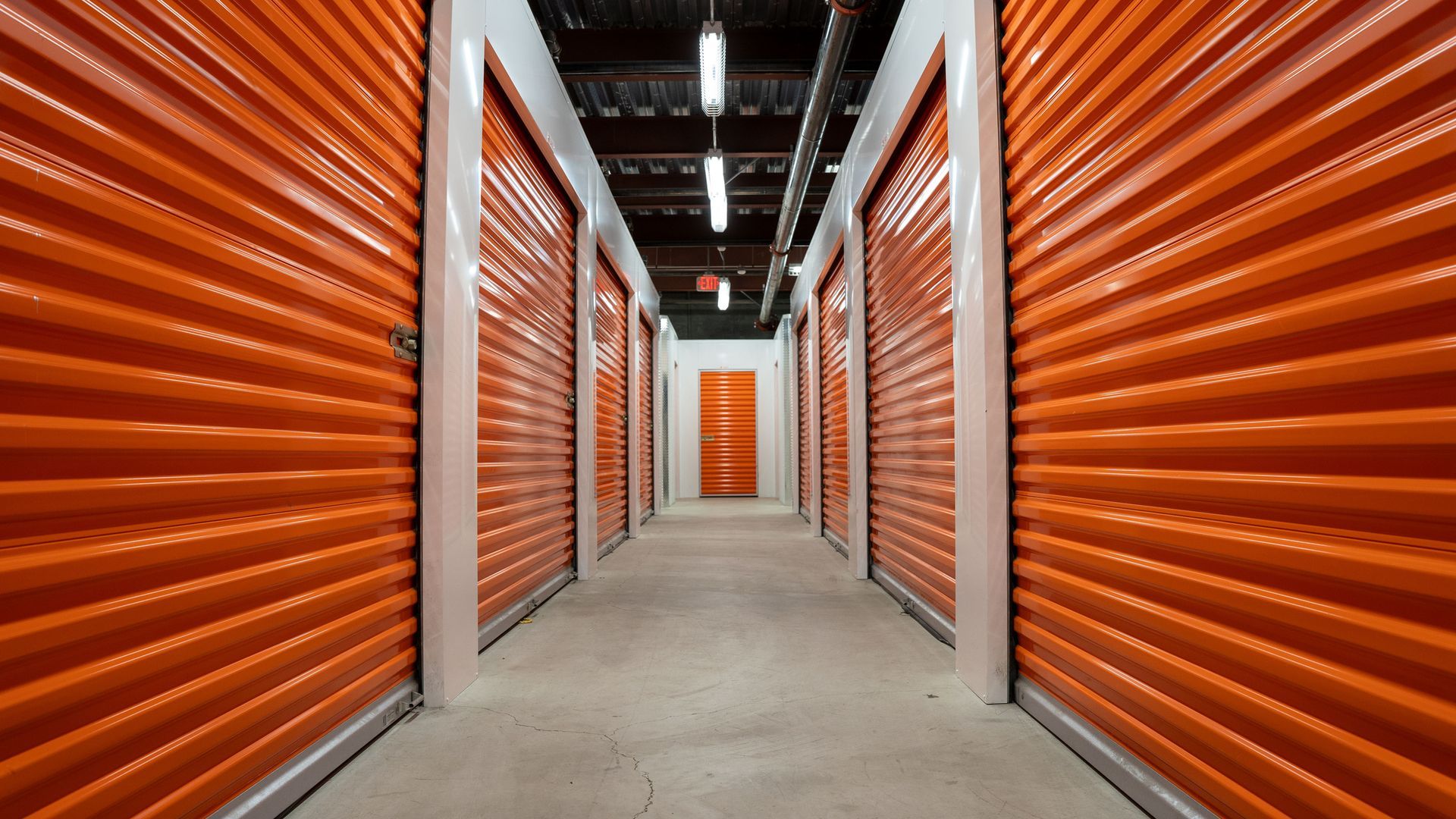 Empty hallway with orange garage doors of a self-storage unit warehouse.