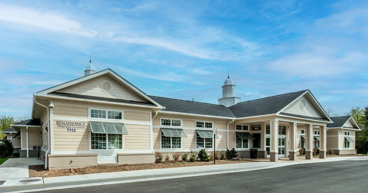 A large white house with a gray roof is sitting on the side of a road.