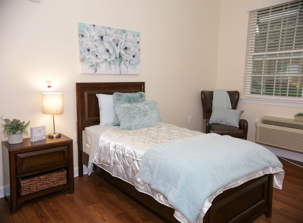 A bedroom with a single bed , nightstand , chair and window.