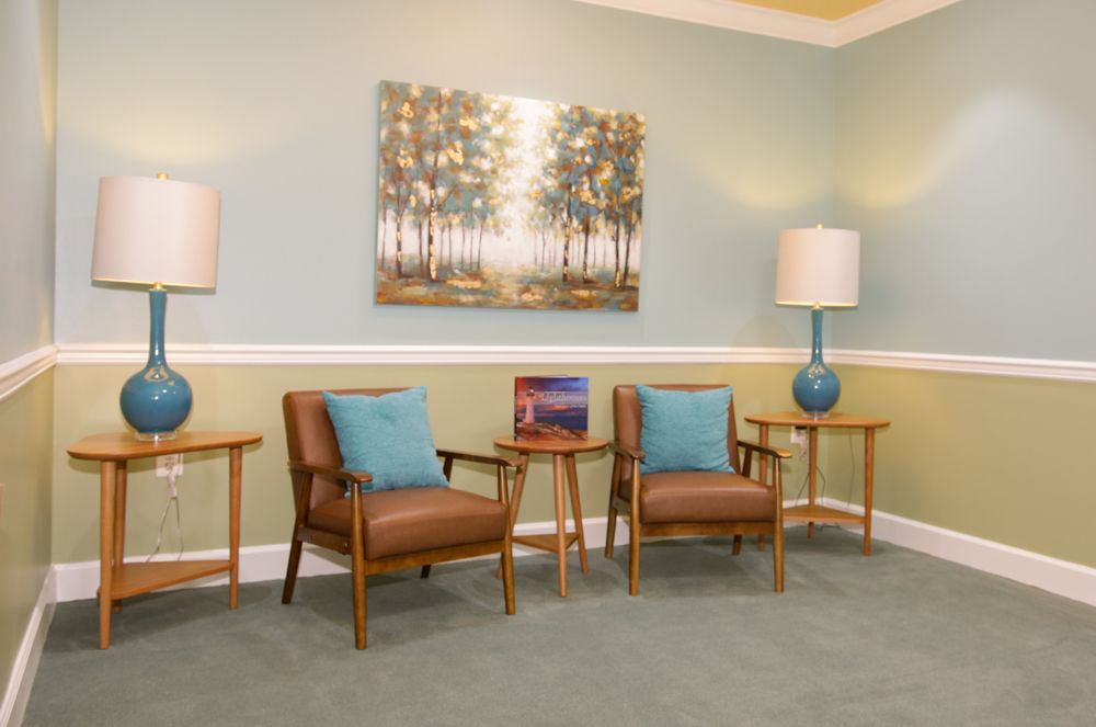 A living room with two chairs , two tables , two lamps and a painting on the wall.