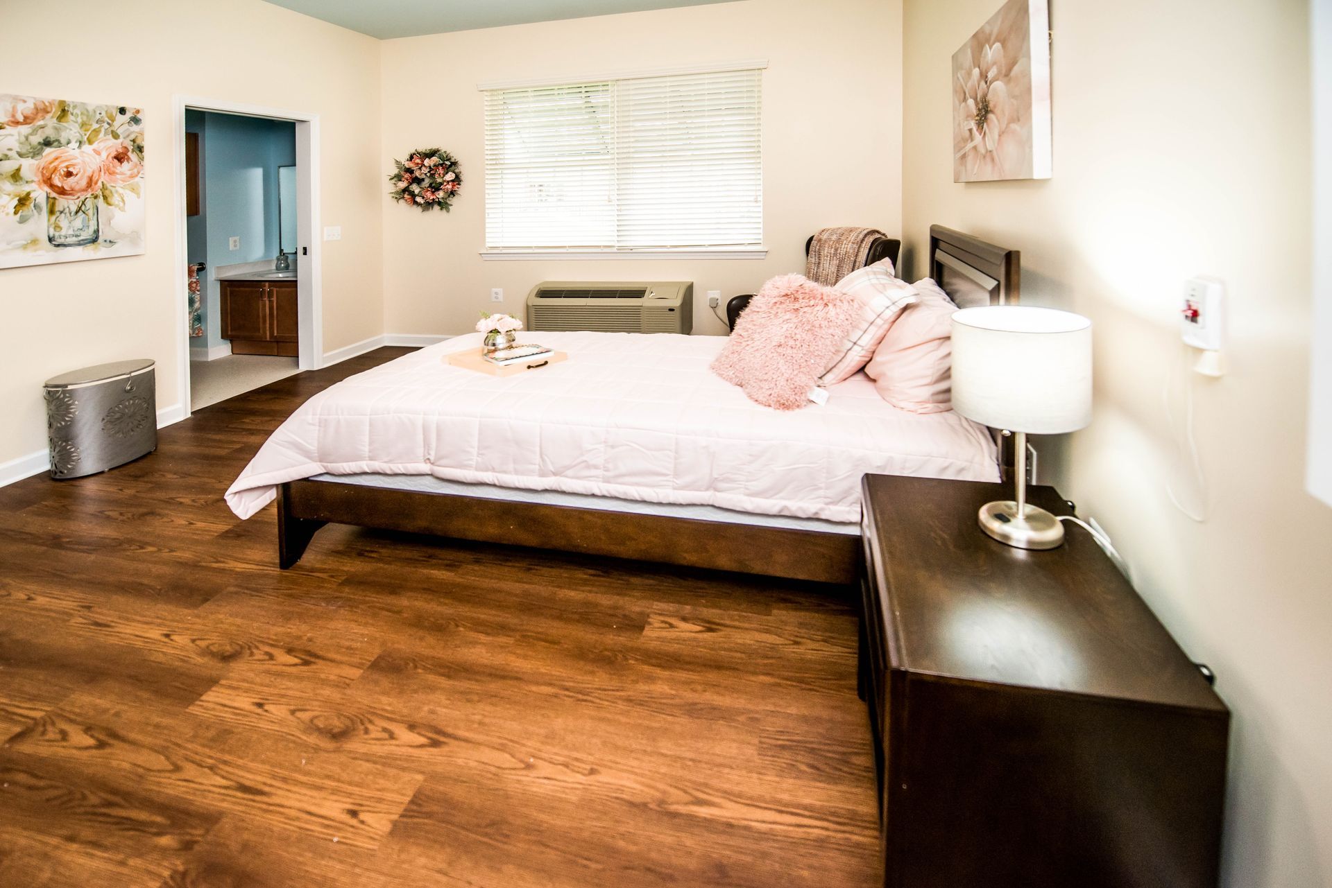 A bedroom with a bed , nightstand , lamp and window.