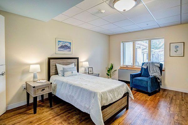A bedroom with a single bed , chair , nightstand and window.