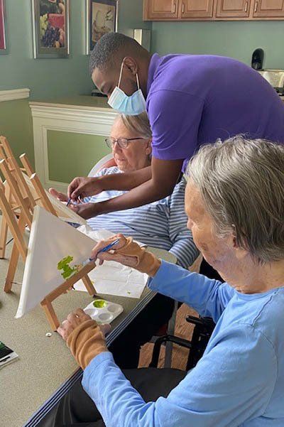 A group of people are sitting at a table painting on easels.