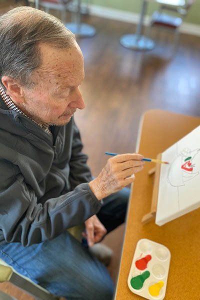 A man is sitting at a table painting a picture on a canvas.