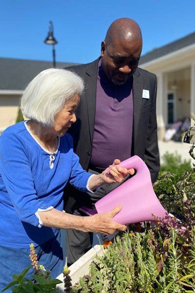 A man and a woman are watering plants in a garden.