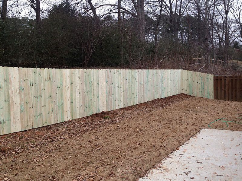 A wooden fence is in the middle of a dirt field.