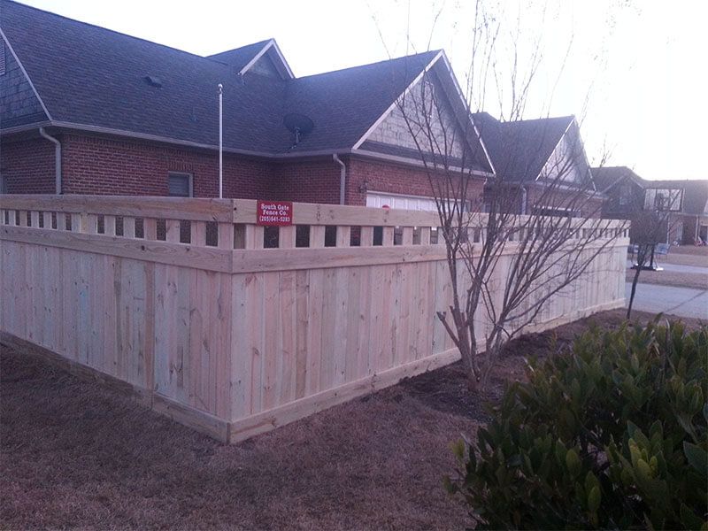 A wooden fence is in front of a brick house.