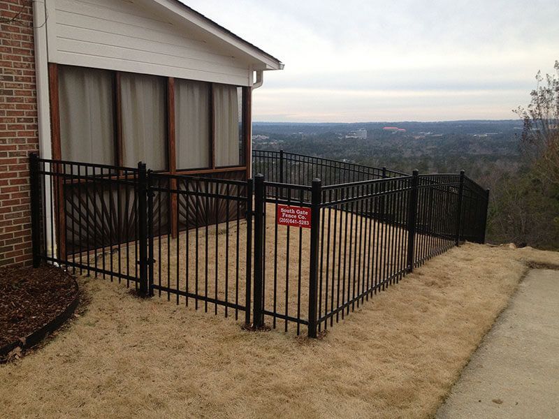 A black wrought iron fence surrounds a grassy area in front of a house
