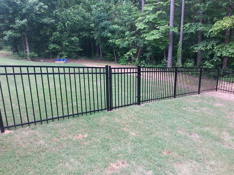 A black metal fence surrounds a lush green field.