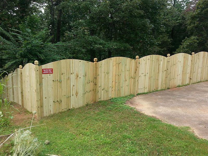 A wooden fence surrounds a driveway in a yard.