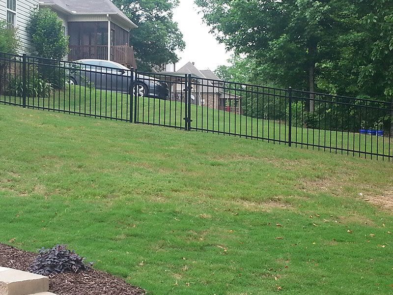 A fence surrounds a lush green lawn in front of a house