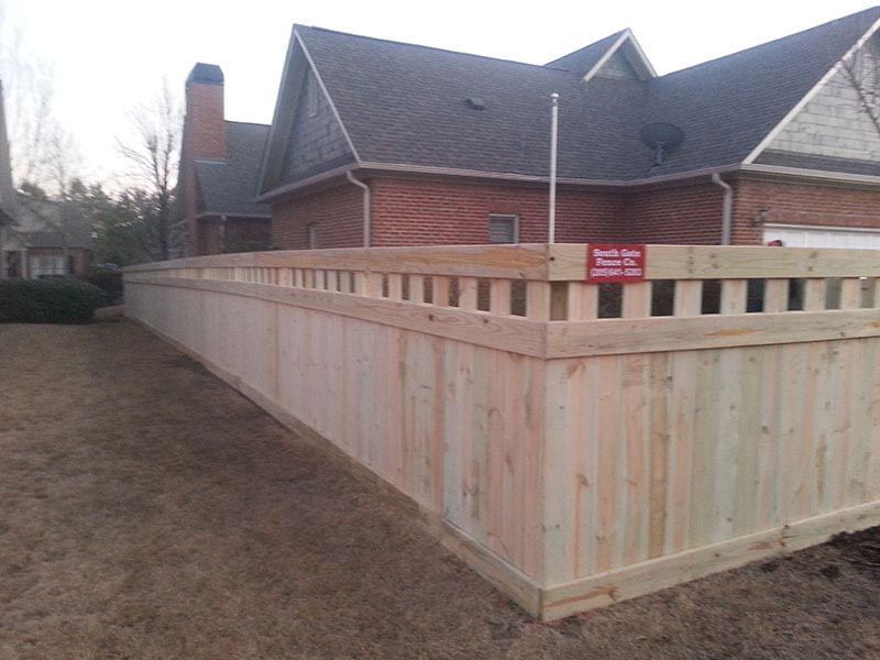 A wooden fence is in front of a brick house.