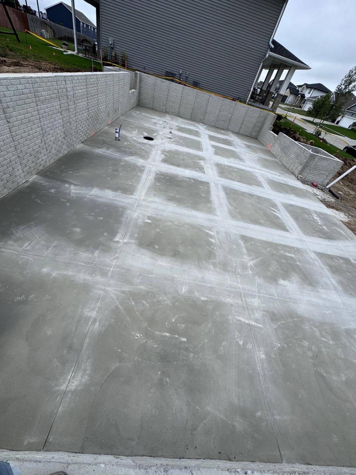 Newly poured concrete driveway with grid pattern, next to a retaining wall and house.