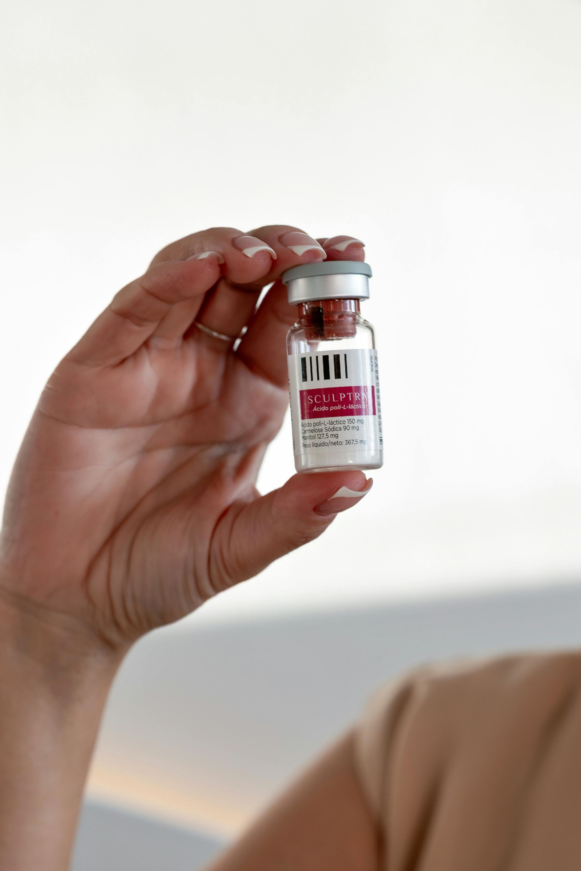 Hand holding a small vial with a red and white label, likely containing medication.