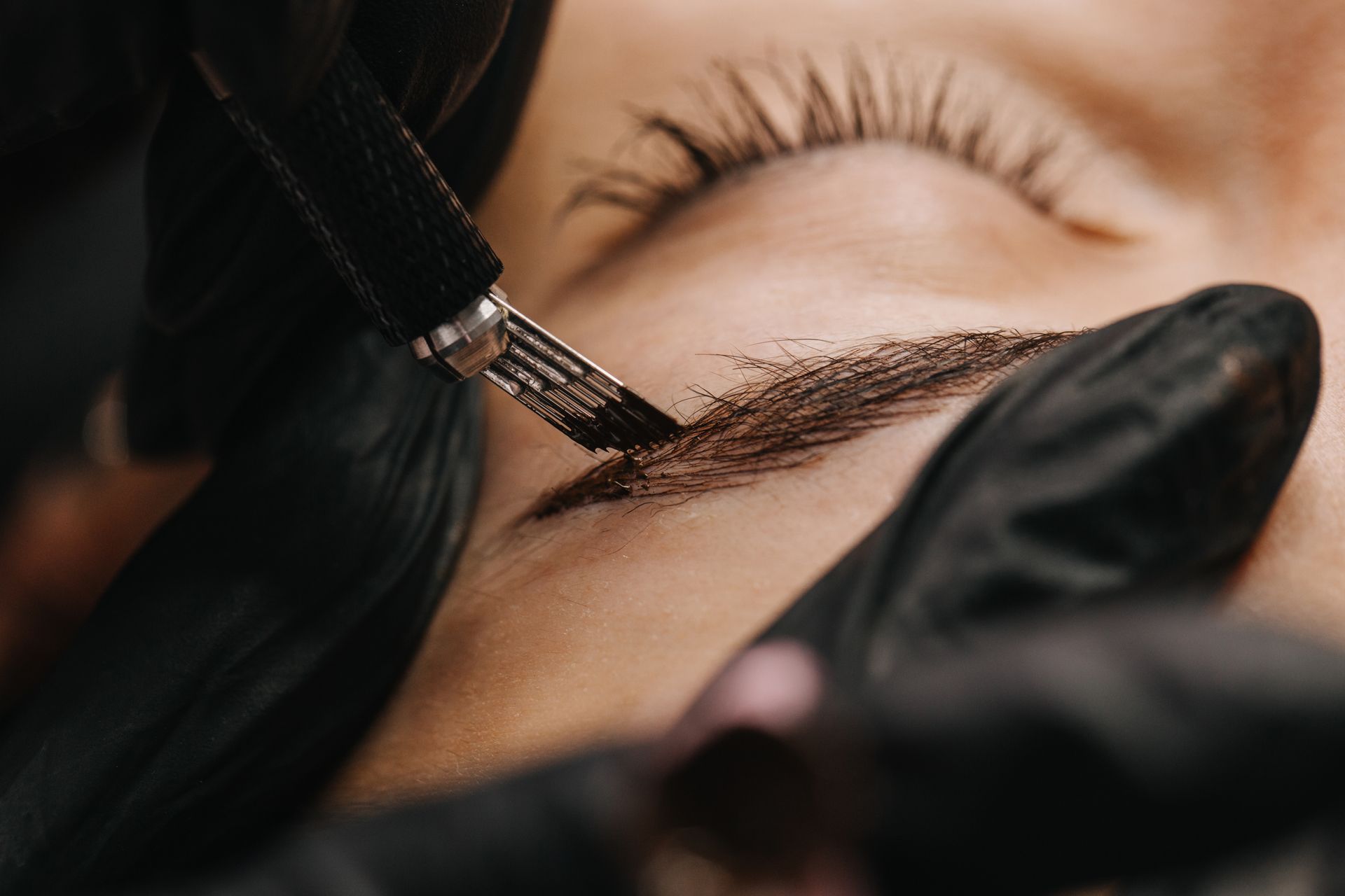 Eyebrow microblading procedure: a tool applies pigment to the eyebrow, close up view.