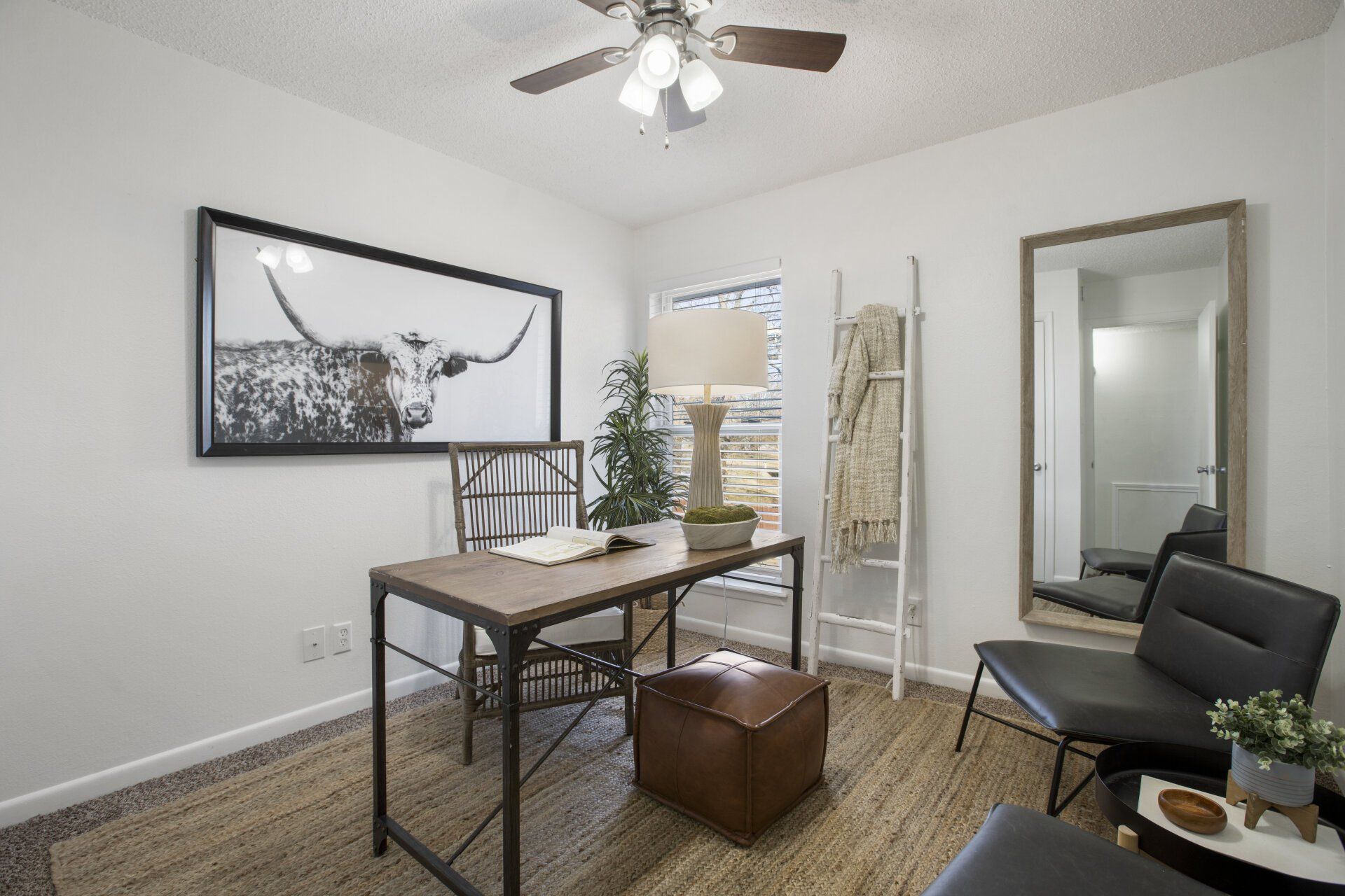 A living room with a desk and chairs and a ceiling fan.