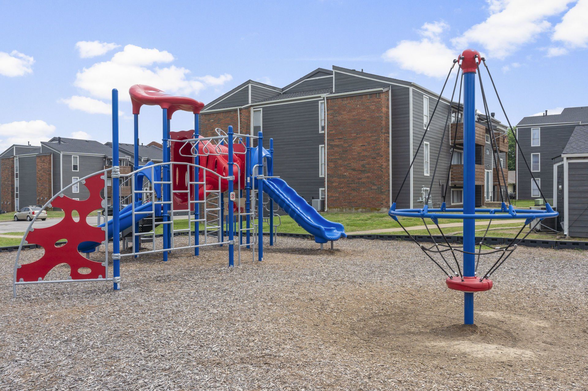 A playground with a slide , ladder , and swings in front of a brick building.