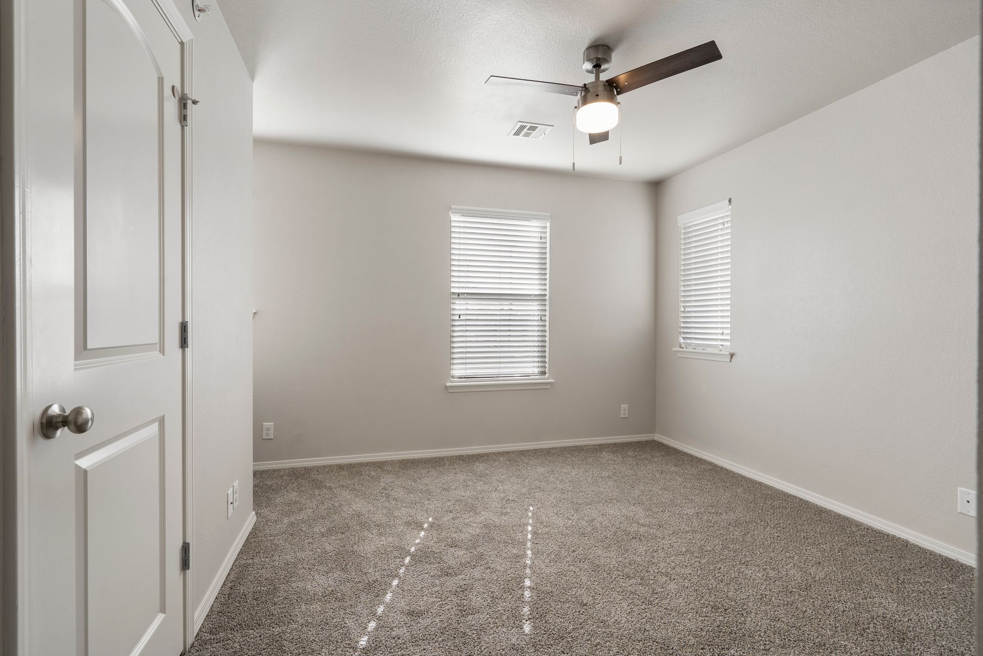 An empty bedroom with a ceiling fan and two windows.