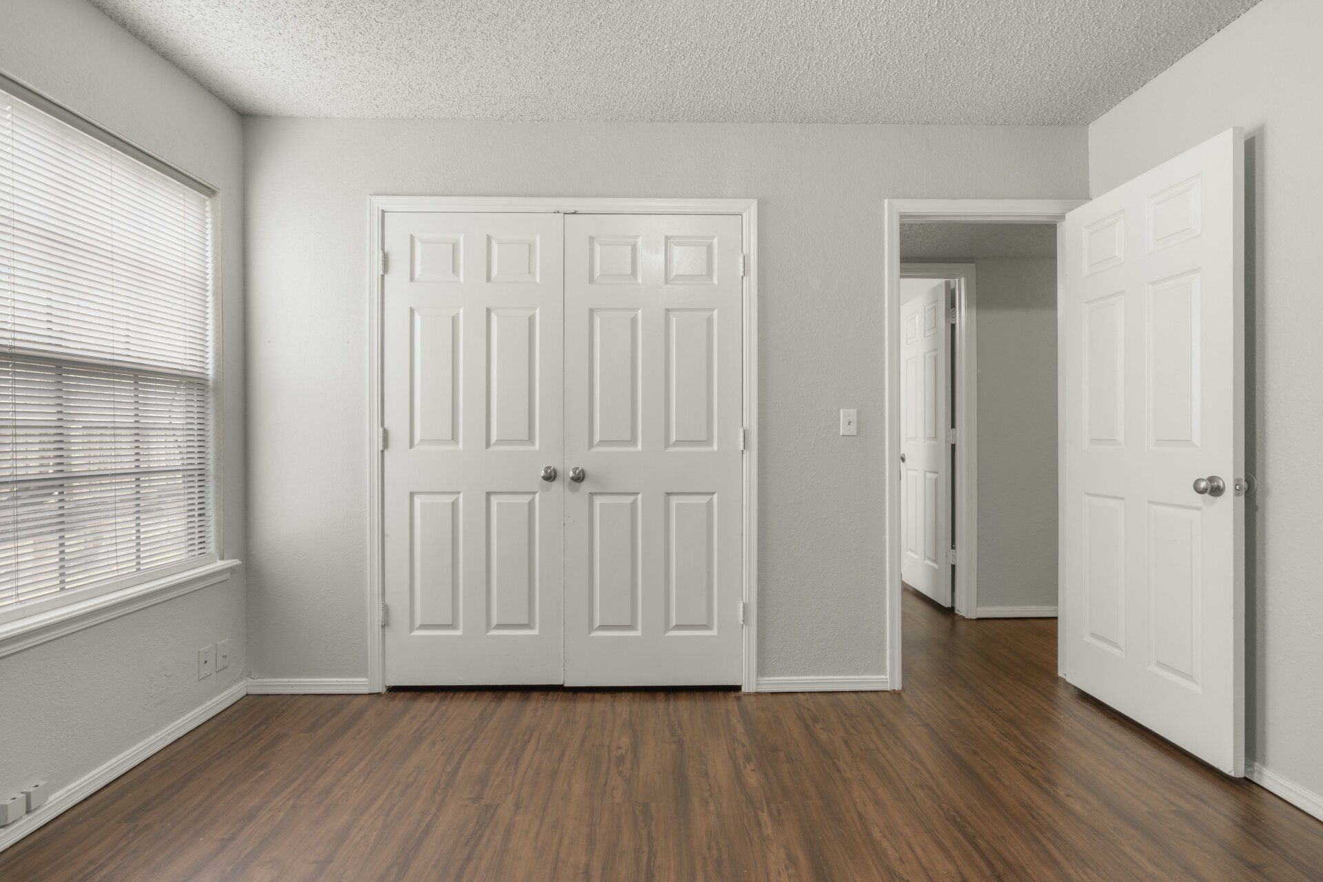 An empty room with hardwood floors and white doors.