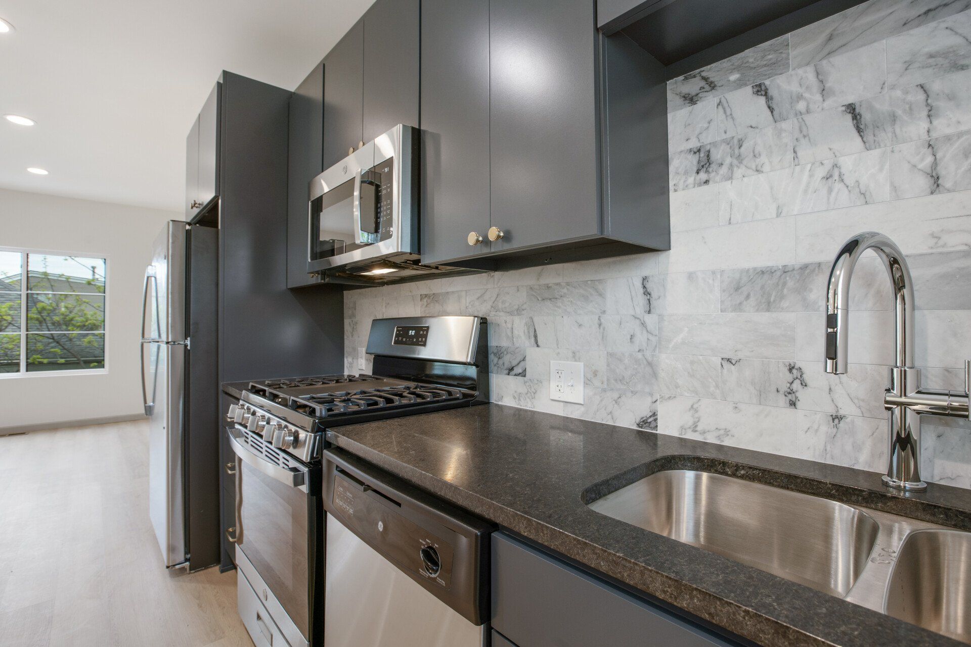 A kitchen with a sink , stove , microwave and refrigerator.