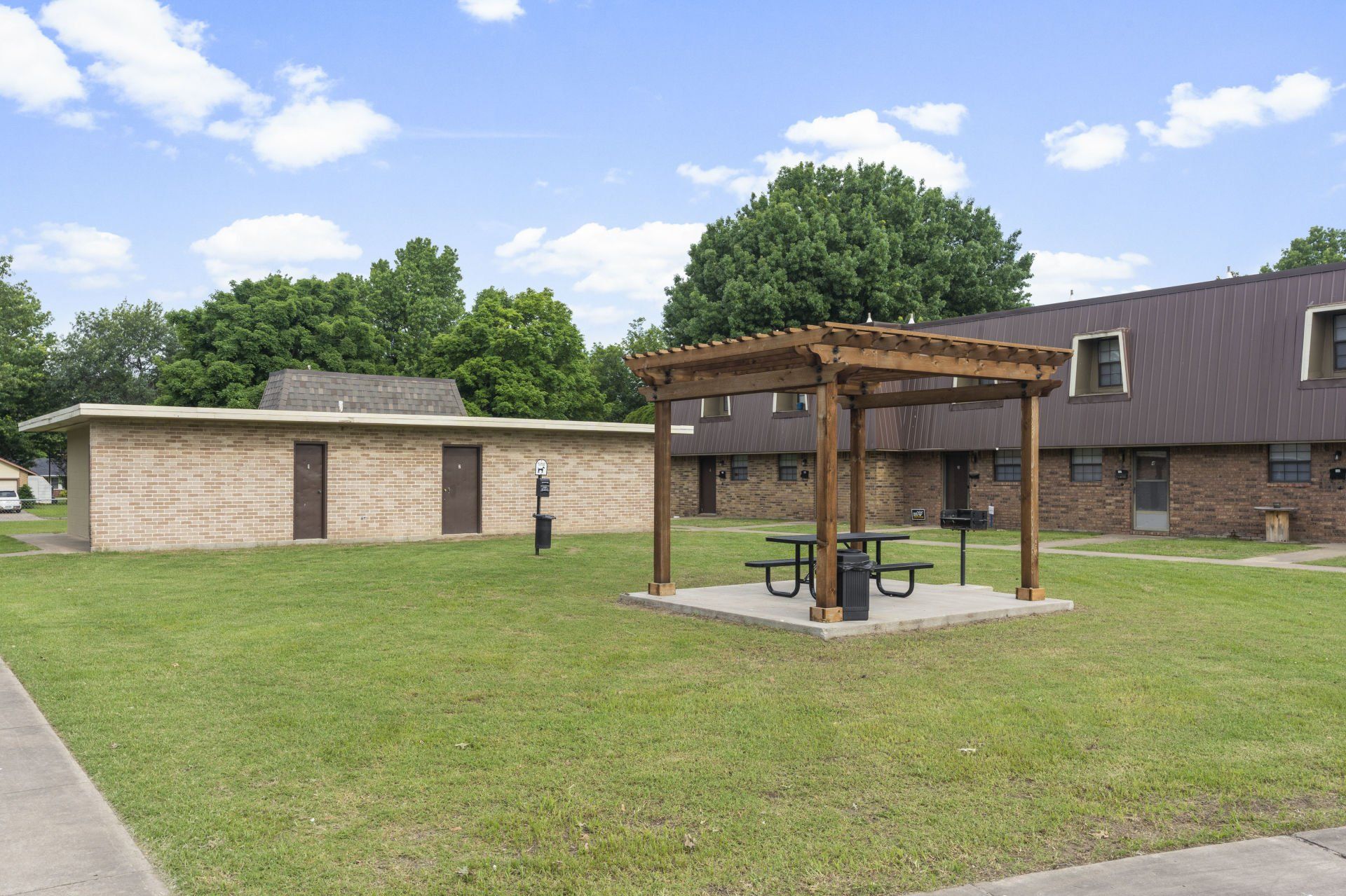 A pergola with a picnic table in front of a brick building.