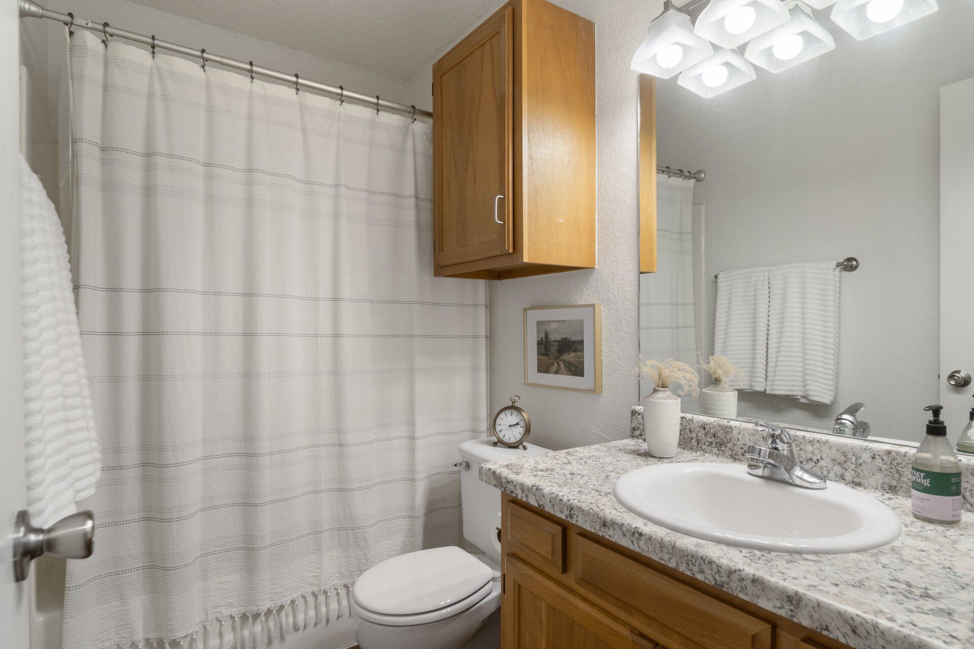 A bathroom with a toilet , sink , mirror and shower curtain.